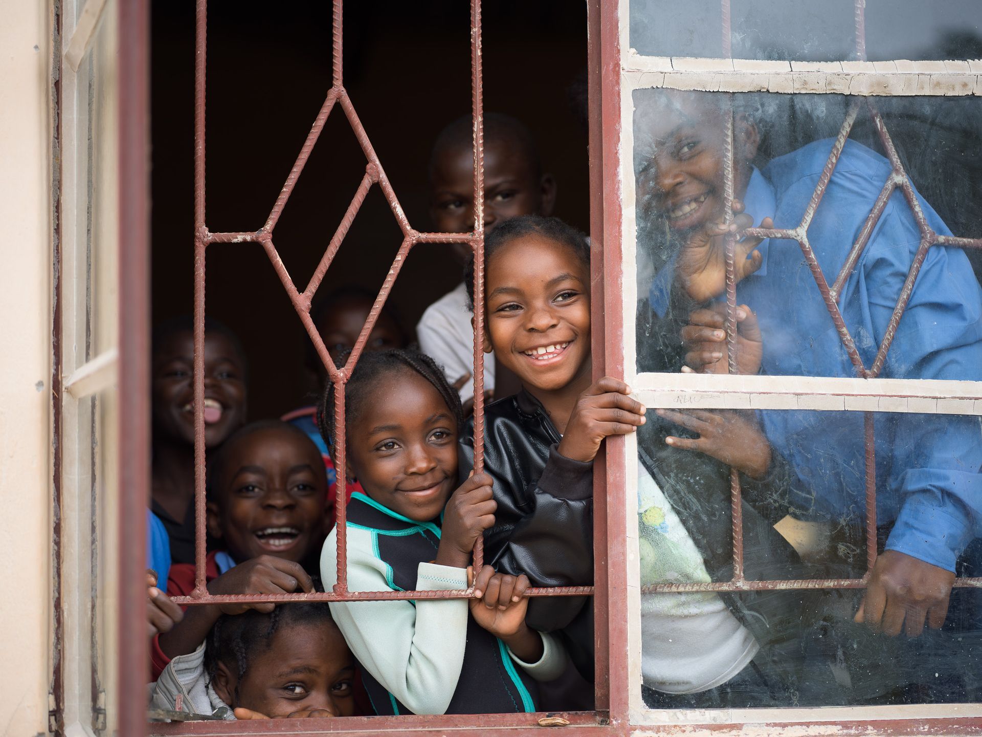 Niños sonriendo a través de una ventana en la escuela comunitaria Road 22, Meheba, Zambia