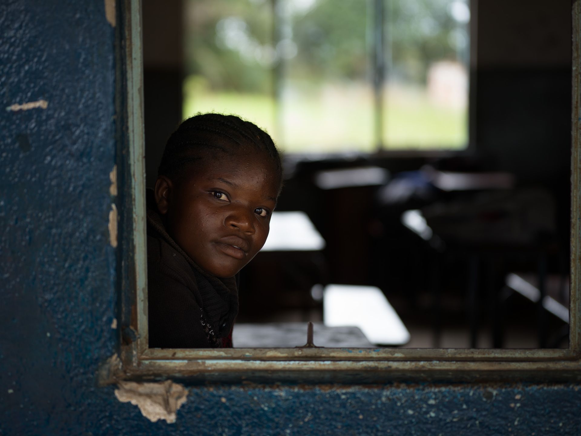 Una niña mira por la ventana de un aula, escuela secundaria Meheba B, Zambia